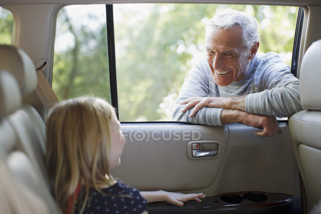 Пожилой мужчина разговаривает с внучкой в окне машины — стоковое фото