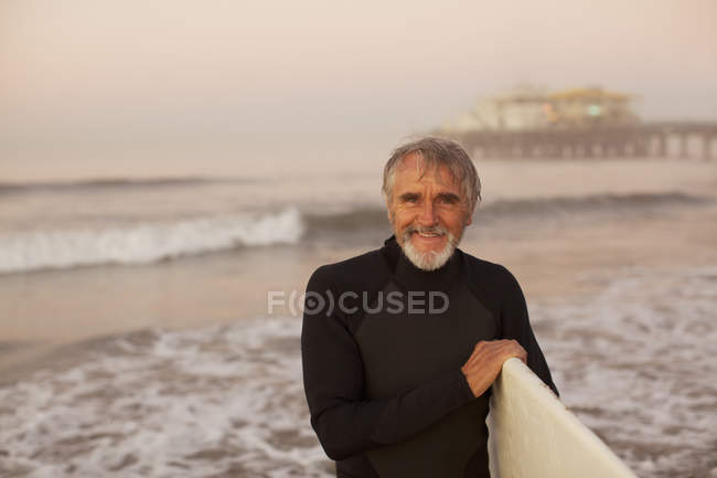 Старий серфер, що несе дошку на пляжі — стокове фото