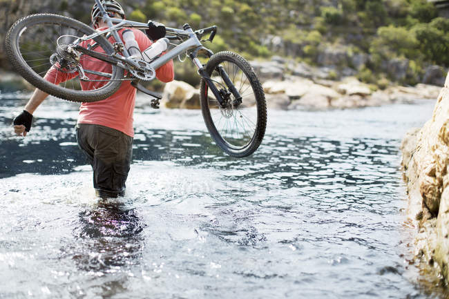 Vue arrière de l'homme portant le vélo de montagne dans la rivière — Photo de stock
