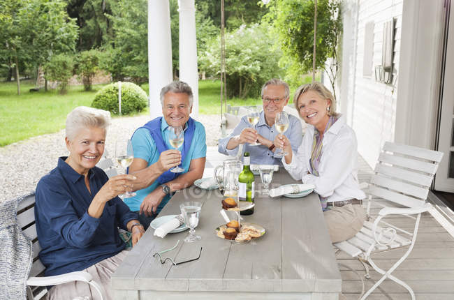 Amigos brindando entre sí con vino en la mesa - foto de stock
