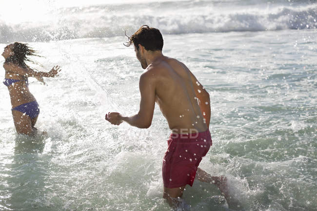 Heureux couple caucasien éclaboussures dans l'océan — Photo de stock