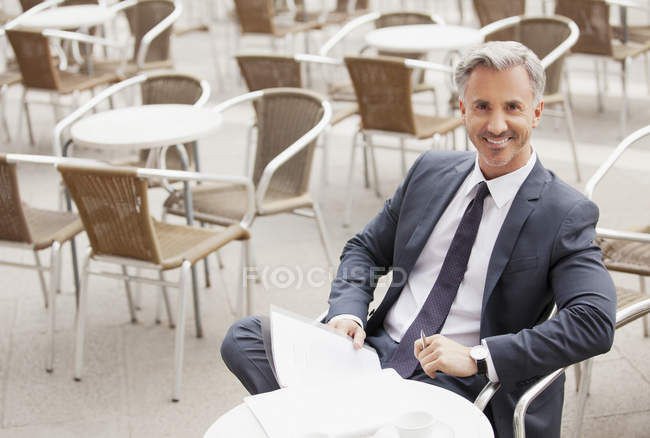 Porträt eines lächelnden Geschäftsmannes mit Papierkram im Straßencafé — Stockfoto