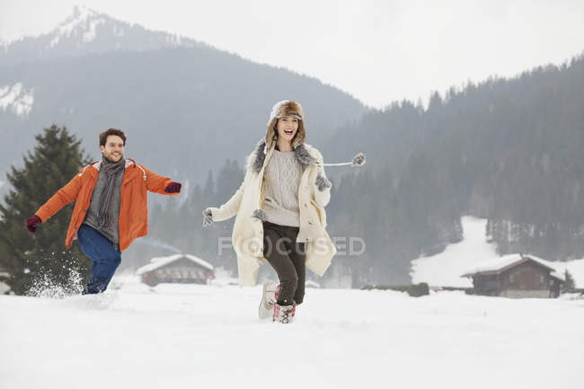 Casal feliz correndo no campo nevado — Fotografia de Stock
