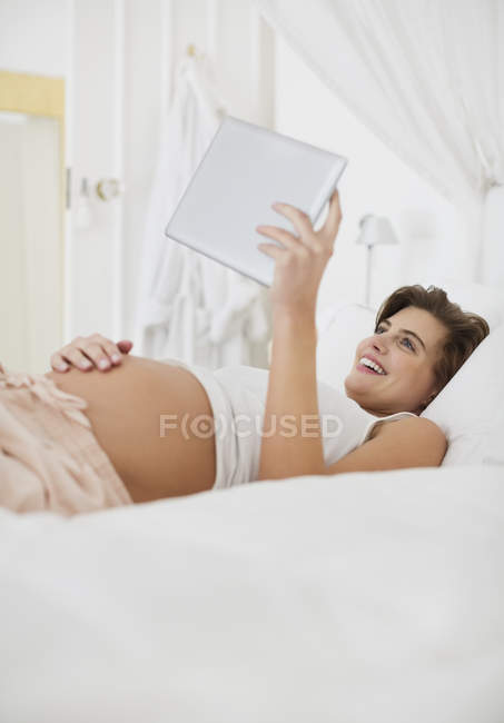 Mulher grávida usando computador tablet na cama — Fotografia de Stock