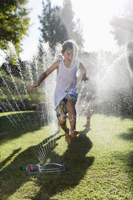 Junge spielt in Sprinkleranlage im Hinterhof — Stockfoto