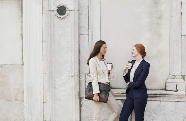 Mulheres de negócios sorridentes bebendo café e falando contra a parede da construção — Fotografia de Stock