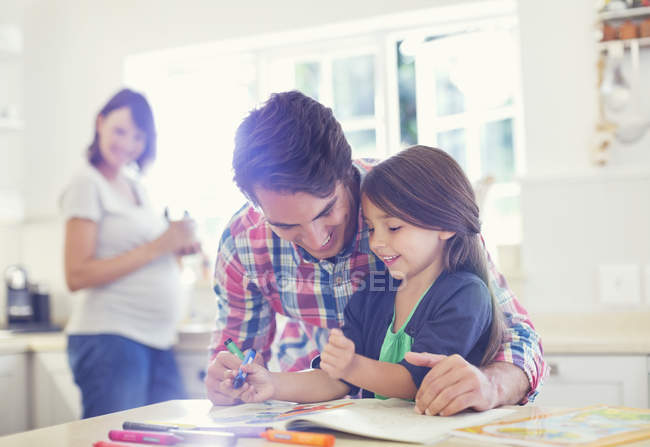 Father helping daughter use coloring book — Stock Photo