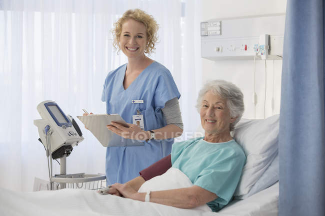 Retrato de enfermera sonriente y paciente mayor en la habitación del hospital - foto de stock