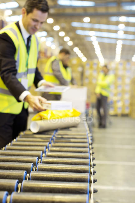 Businessman checking packages on conveyor belt in warehouse — Stock Photo