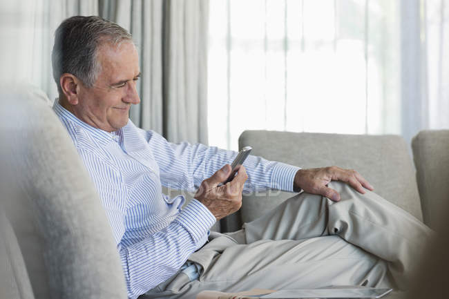 Homem mais velho usando telefone celular no sofá — Fotografia de Stock