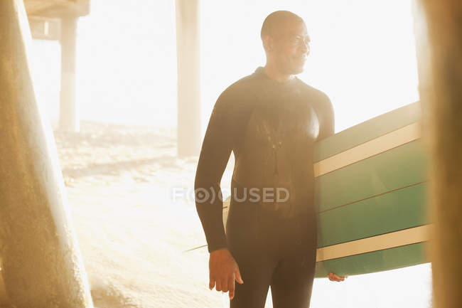 Surfista mayor llevando tabla debajo del muelle - foto de stock