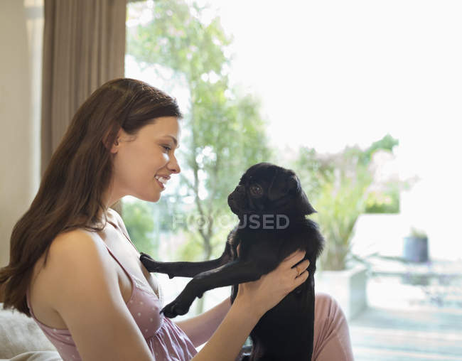 Smiling woman holding dog on bed — Stock Photo