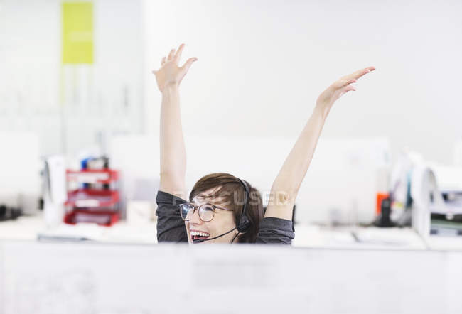 Businesswoman in headset cheering at desk at modern office — Stock Photo