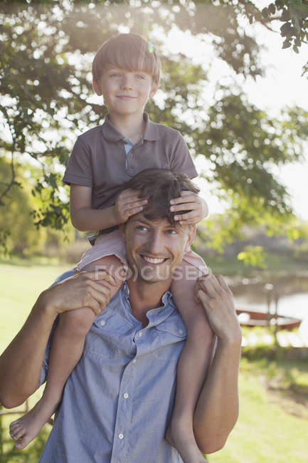 Отец носит улыбающегося сына на плечах у озера — стоковое фото