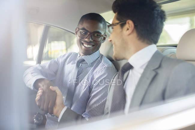 Hombres de negocios sonrientes dándose la mano en el coche - foto de stock