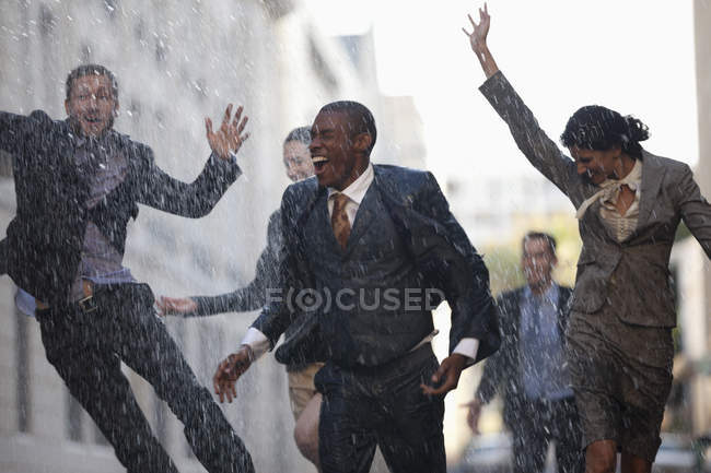 Empresários entusiasmados correndo na rua chuvosa — Fotografia de Stock