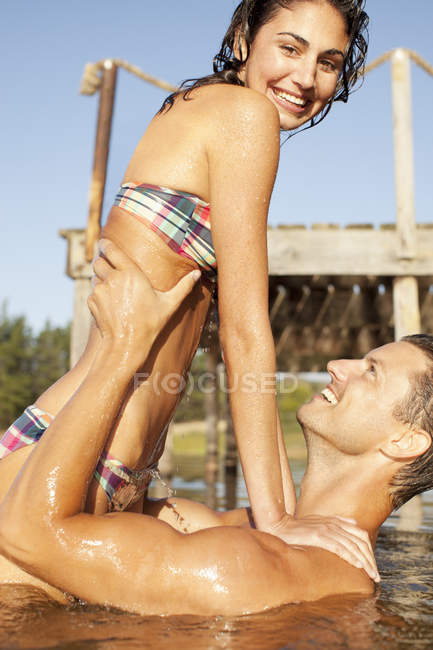 Мужчина поднимает улыбающуюся женщину в озере — стоковое фото