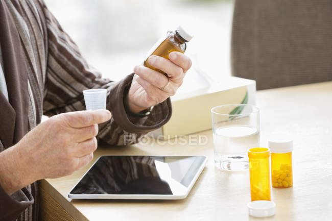Пожилой мужчина принимает лекарства за столом — стоковое фото