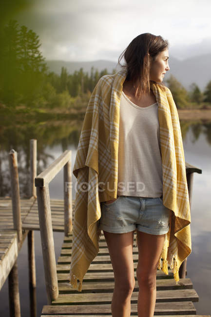 Женщина, завернутая в одеяло, стоит на причале над озером — стоковое фото