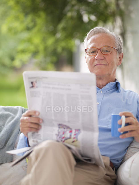 Человек, читающий газету на крыльце — стоковое фото
