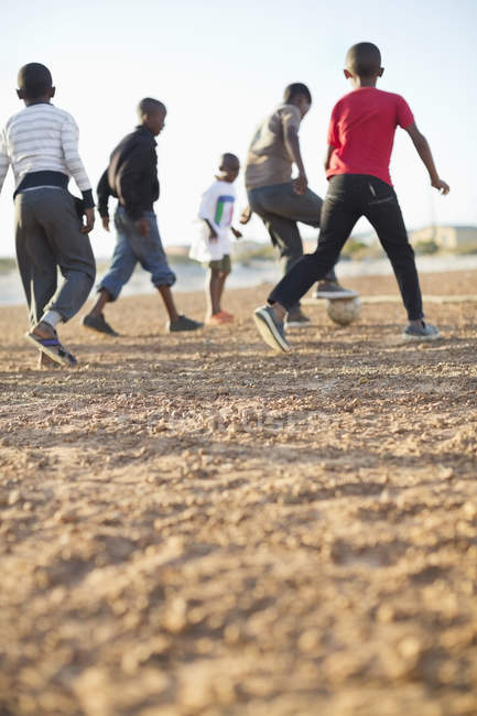 Chicos africanos jugando al fútbol juntos en el campo de tierra - foto de stock