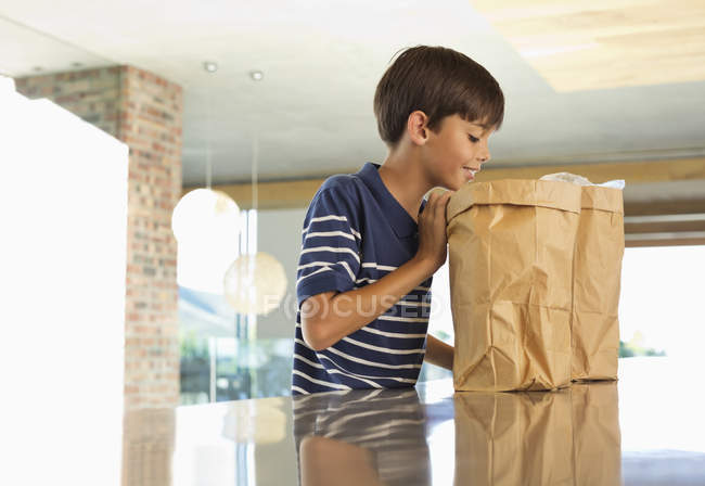 Niño mirando a través de bolsa de papel en la cocina - foto de stock