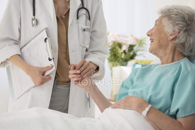 Médico y paciente anciano tomados de la mano en el hospital - foto de stock