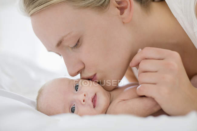 Мать целует новорожденного ребенка в постели — стоковое фото