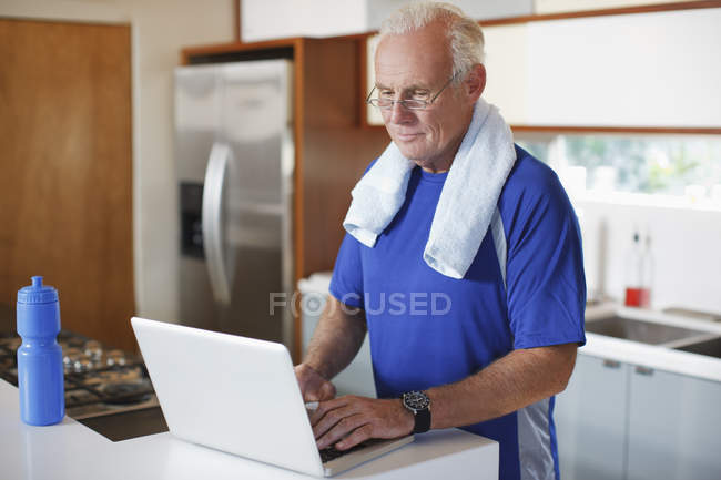 Hombre mayor usando el ordenador portátil después del entrenamiento - foto de stock