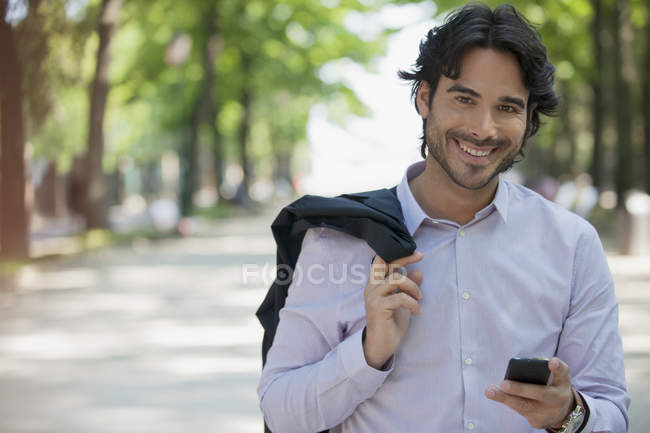 Портрет усміхненого чоловіка, що тримає мобільний телефон у парку — стокове фото