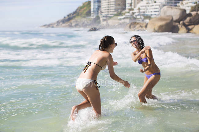 Playful friends in bikinis splashing in ocean — Stock Photo