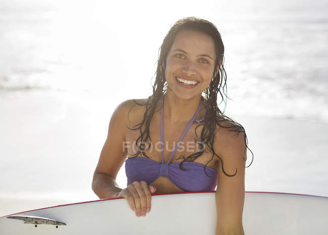 Портрет усміхненої жінки, що тримає дошку для серфінгу на пляжі — стокове фото