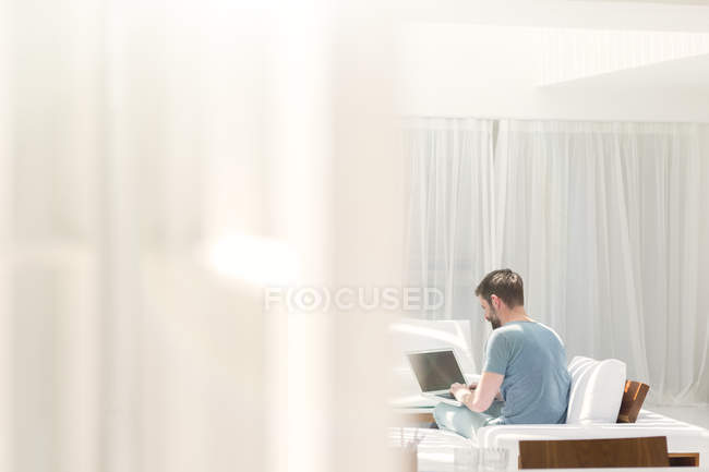 Человек с ноутбуком на диване в современной гостиной — стоковое фото