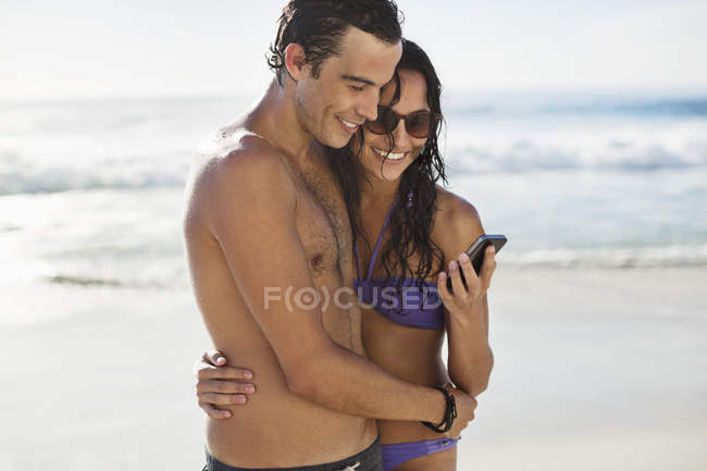 Coppia felice con cellulare che si abbraccia sulla spiaggia — Foto stock