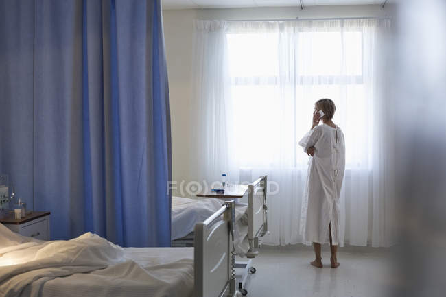 Paciente en bata hablando por celular en la habitación del hospital - foto de stock