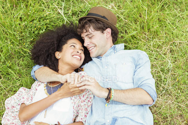 Happy couple holding hands and laying in grass — Stock Photo