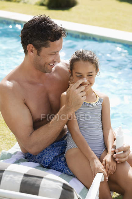 Vater sprüht Tochter am Pool Sonnencreme auf die Nase — Stockfoto