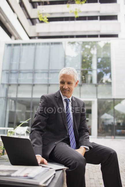 Empresário usando laptop no banco fora do prédio de escritórios — Fotografia de Stock