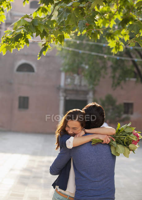 Mujer sosteniendo flores y abrazando al hombre - foto de stock