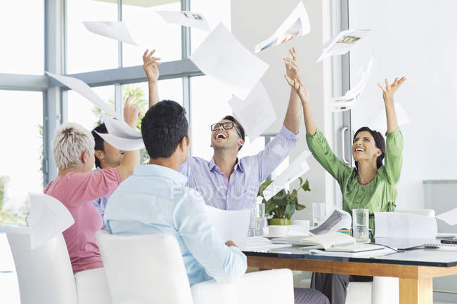 Business people tossing papers in air in meeting — Stock Photo