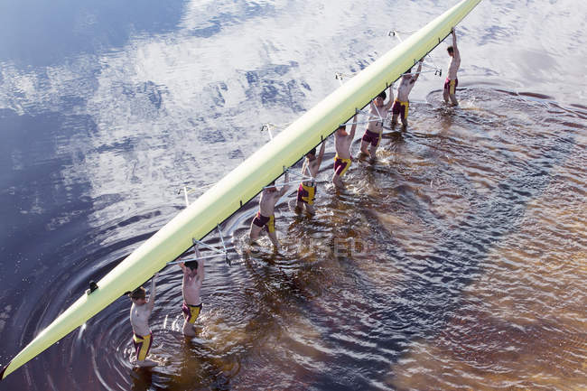 Rowing crew carrying scull overhead in lake — Stock Photo