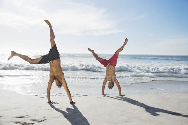 Men in swim trunks doing handstands on beach — Stock Photo