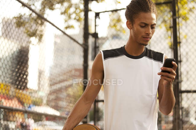 Hombre usando el teléfono celular en la cancha de baloncesto - foto de stock