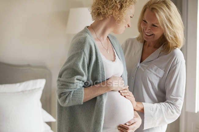 Sonriente madre tocando el estómago de la hija embarazada - foto de stock