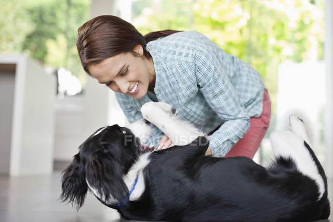 Улыбающаяся женщина играет с собакой в современном доме — стоковое фото