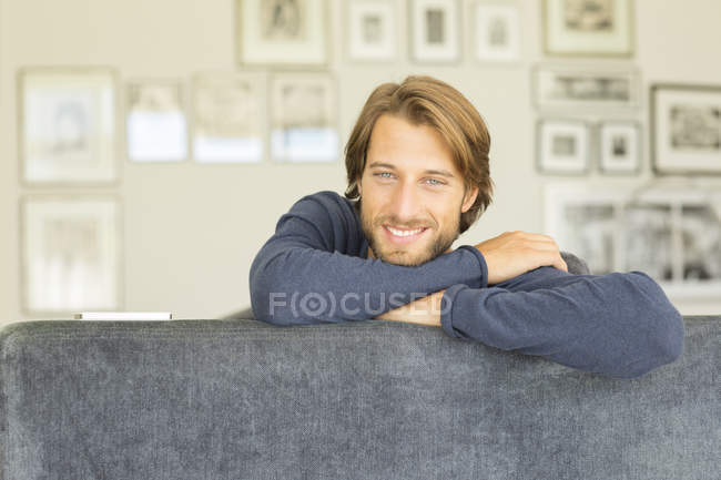 Junger attraktiver lächelnder Mann sitzt auf Sofa — Stockfoto