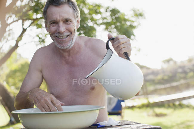 Porträt eines lächelnden Mannes mit Krug-Waschgesicht im Becken am Seeufer — Stockfoto
