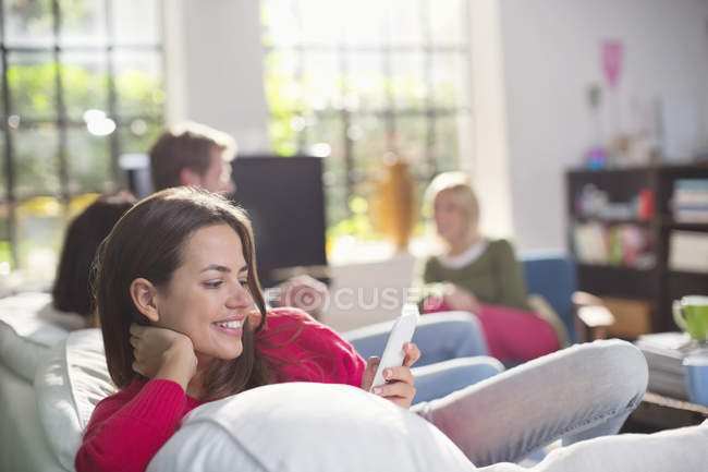 Усміхнена жінка використовує мобільний телефон на дивані — стокове фото
