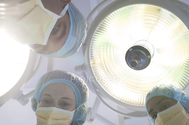 Cirujanos inclinados sobre el paciente en la mesa de operaciones - foto de stock