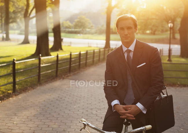 Empresário sentado em bicicleta no parque urbano — Fotografia de Stock